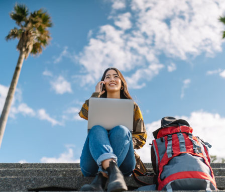 Woman talking on phone while on laptop, outside around palm trees