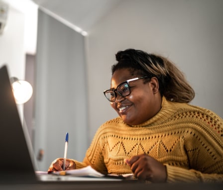 Woman smiling at laptop while writing