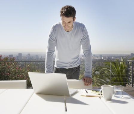 Man working on laptop on balcony with Los Angeles skyline in background