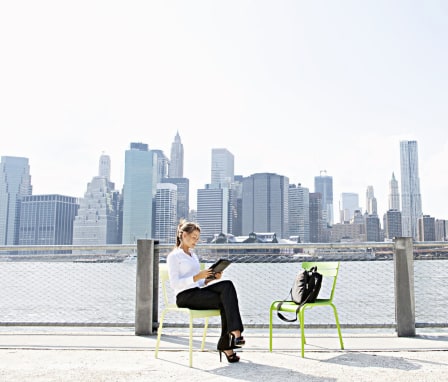 Woman outside on tablet with NYC skyline in background