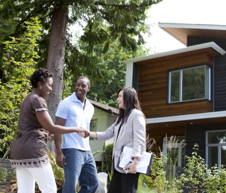 Real estate agent shaking hands and talking to family outside of a house