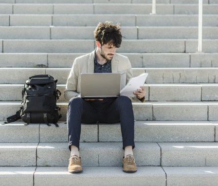 Man sitting on steps outside working on laptop