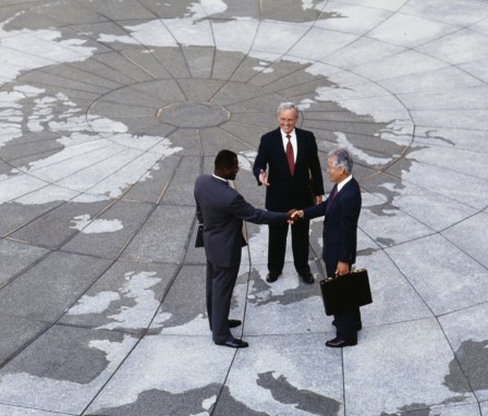 Three business men shaking hands, standing on concrete printed like a globe