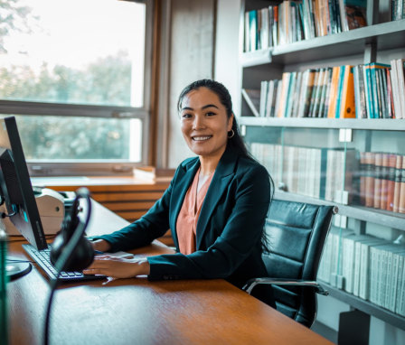 Woman working on a computer at a desk with a full bookshelf behind her