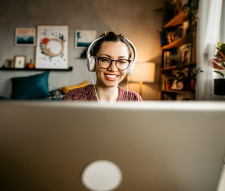 Young woman smiling and using laptop while wearing headphones