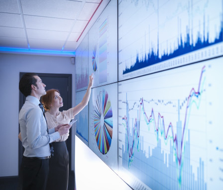 Two colleagues looking at multiple screens showing different types of charts and graphs