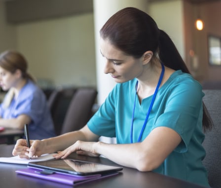 Nursing students wearing scrubs and taking notes in class