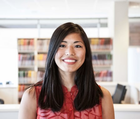 Female Asian-American medical coder smiles while standing in front of her workspace at a medical office.