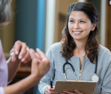 Filipino-American female psychiatric mental health nurse practitioner talking to a senior patient during an appointment. The nurse is taking notes in the patient's chart.