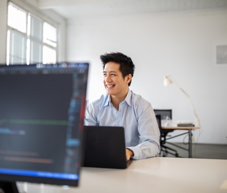 Man coding on laptop beside monitor in office