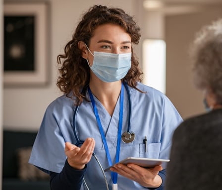 Masked nurse talking to senior patient while holding tablet