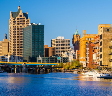 Milwaukee downtown (including 100 East Wisconsin, the tallest building in view), a highway, a river, and boats, during the late afternoon.