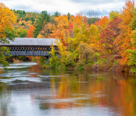 New England College's Henniker Covered Bridge, surrounded by peak fall foliage, along the Contoocook River in Henniker, New Hampshire.