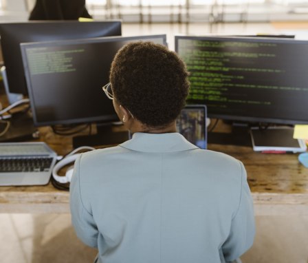 Rear view of female programmer working on computer at desk in creative office