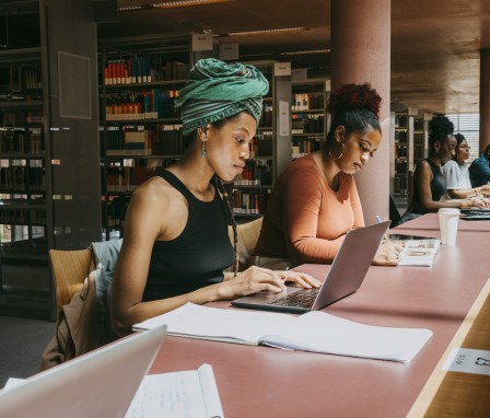 Woman wearing turban using laptop while sitting with friend in library