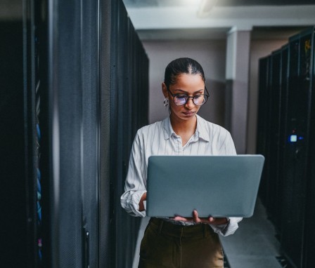 Shot of a young woman using a laptop while working in a server room