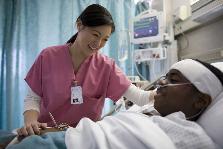 Nursing assistant checks in on a young male patient lying in bed in a hospital.