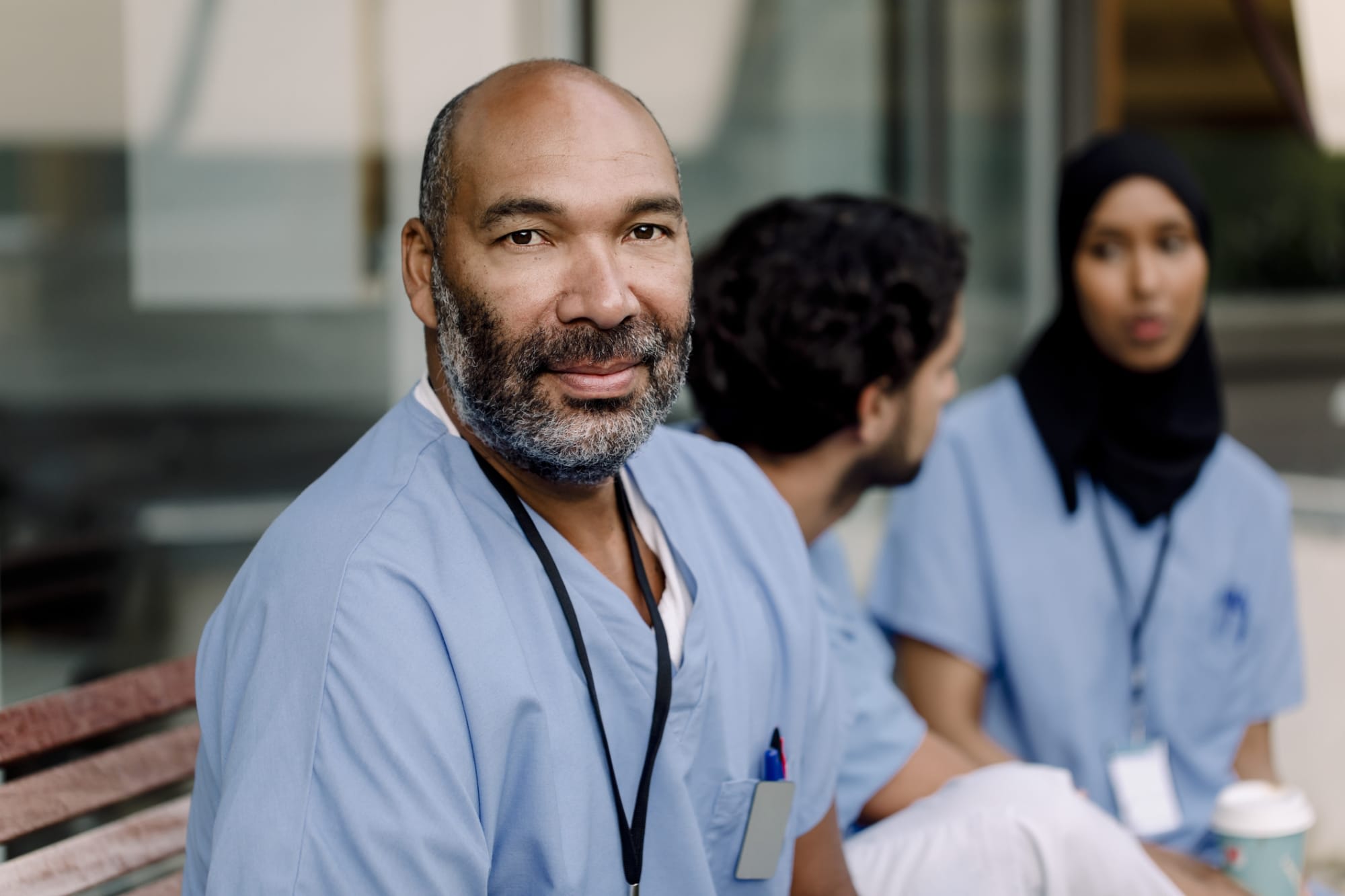 black male nurse looking directly at camera with two other nurses talking together in the background