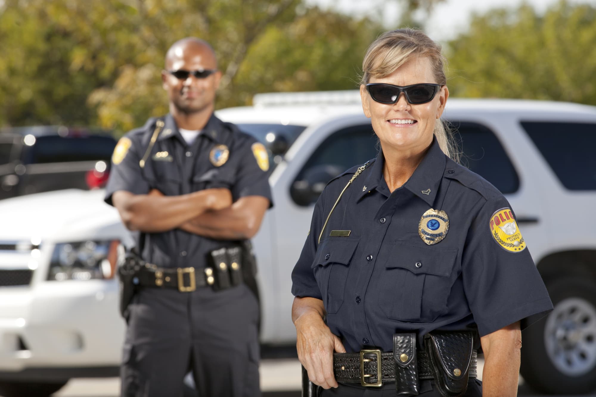 Two police officers smiling by a police car