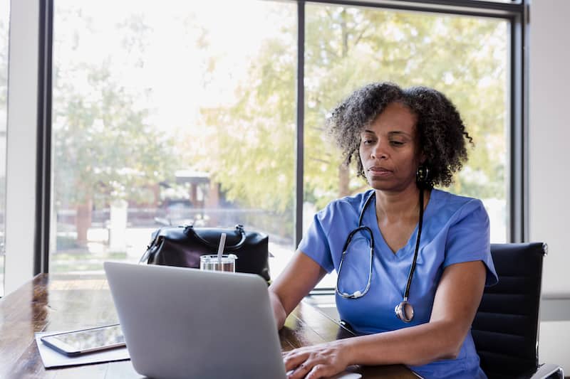 Nurse typing on laptop beside window