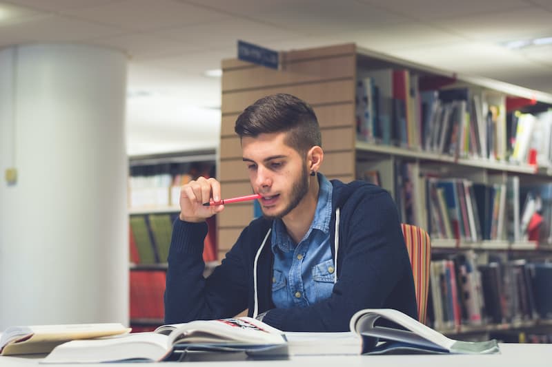 Young man studying textbook in library