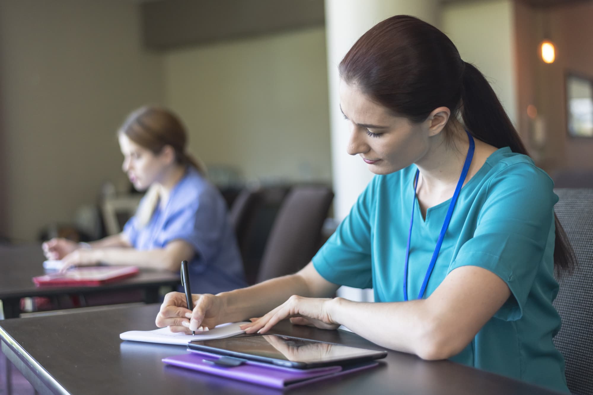 Nursing students wearing scrubs and taking notes in class