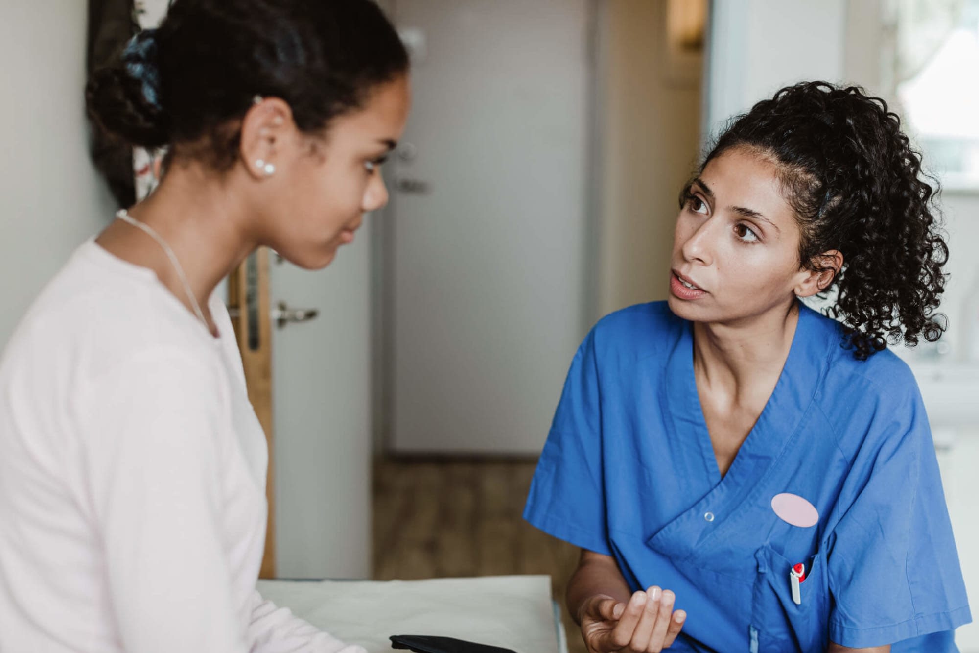 Female women's health nurse practitioner discussing with a young female patient in a medical room at a small clinic.