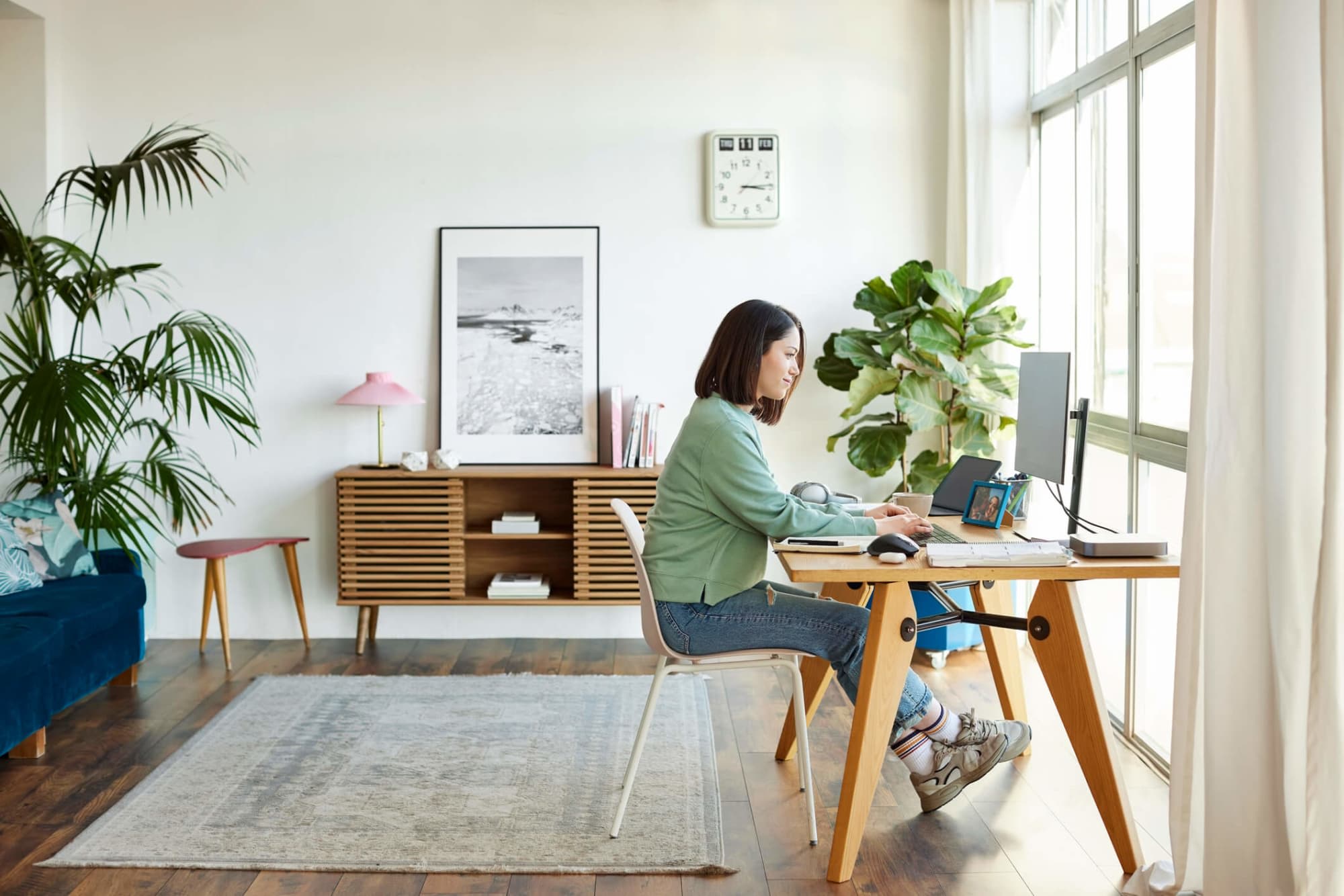 A mid-adult Hispanic woman typing on her computer at home. She is dressed casually in a sweater and jeans, and is sitting at a table in her home office.