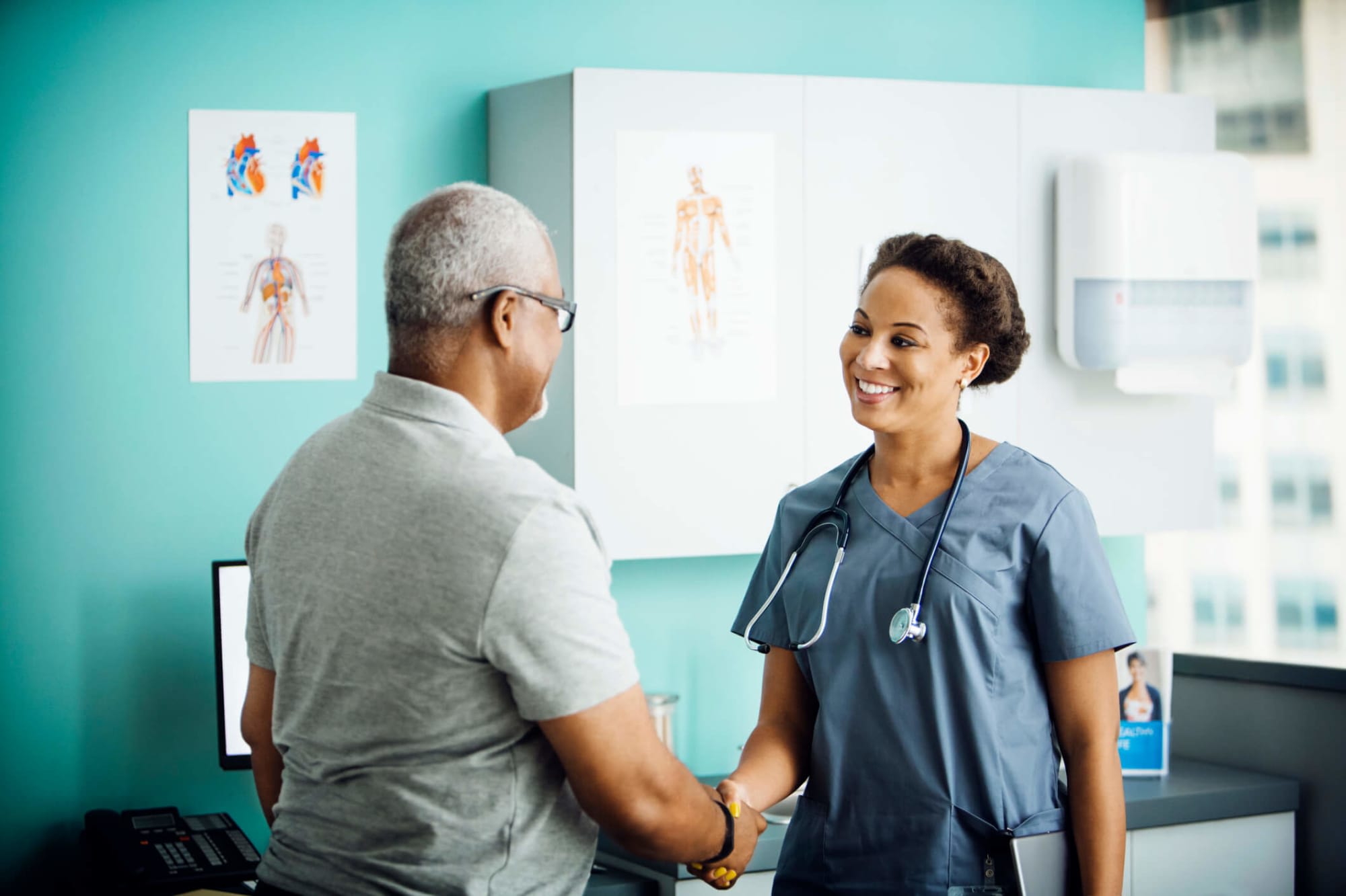 Smiling Black female nurse greets a senior male patient in a family practice clinic.