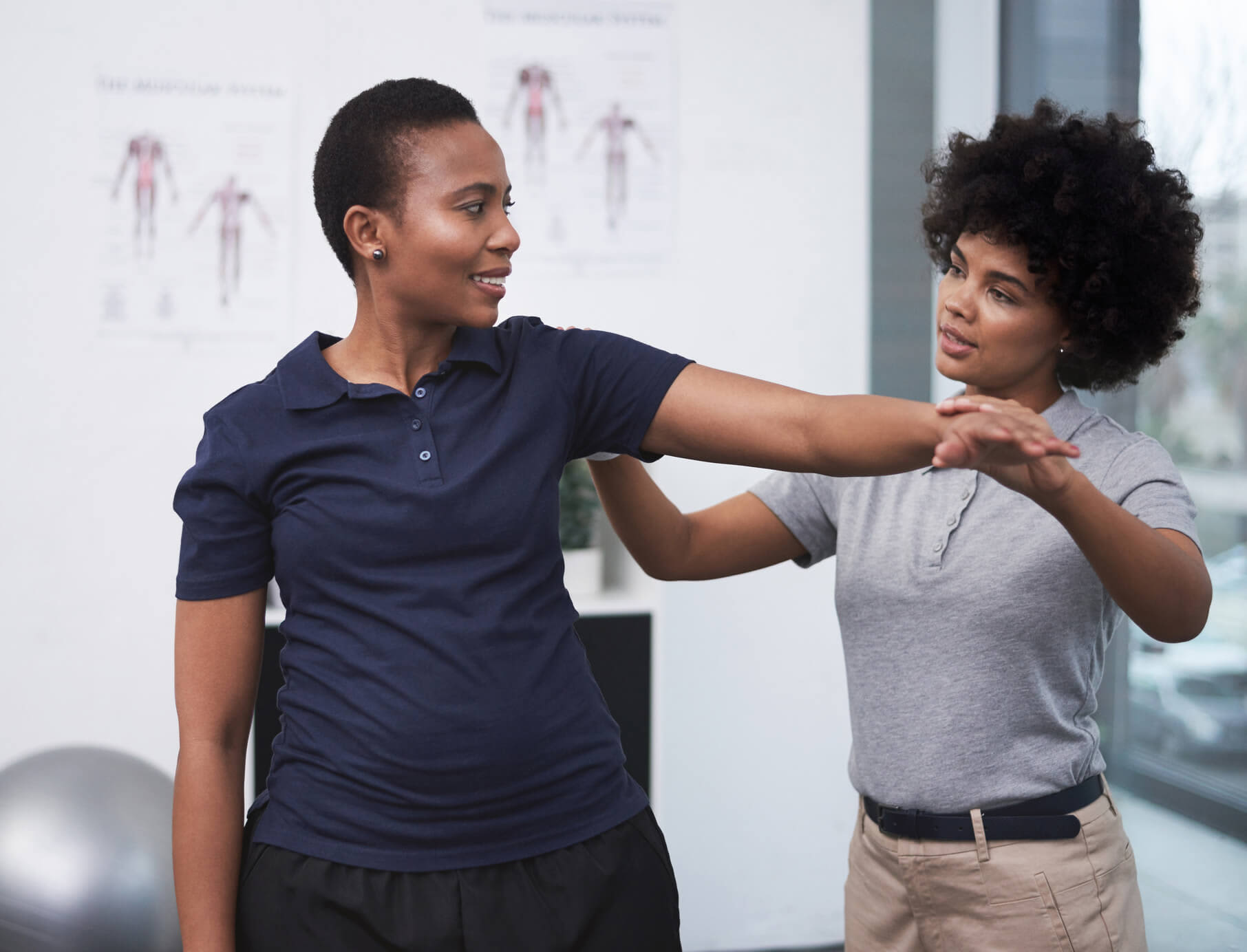 A Black female physical therapist is helping her senior patient with arm exercises during a physical therapy session.