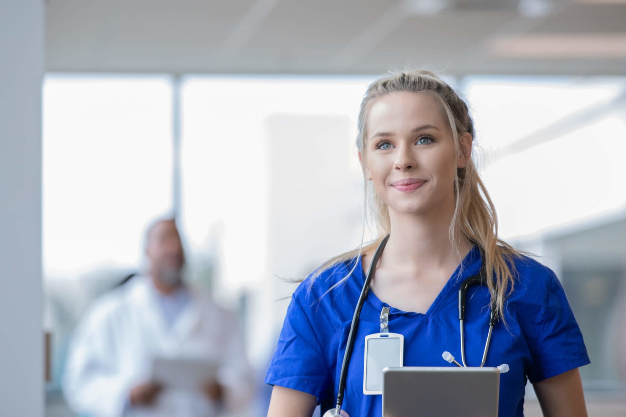 Young female medical assistant walking through a hospital hallway, holding a patient's file in her hand.