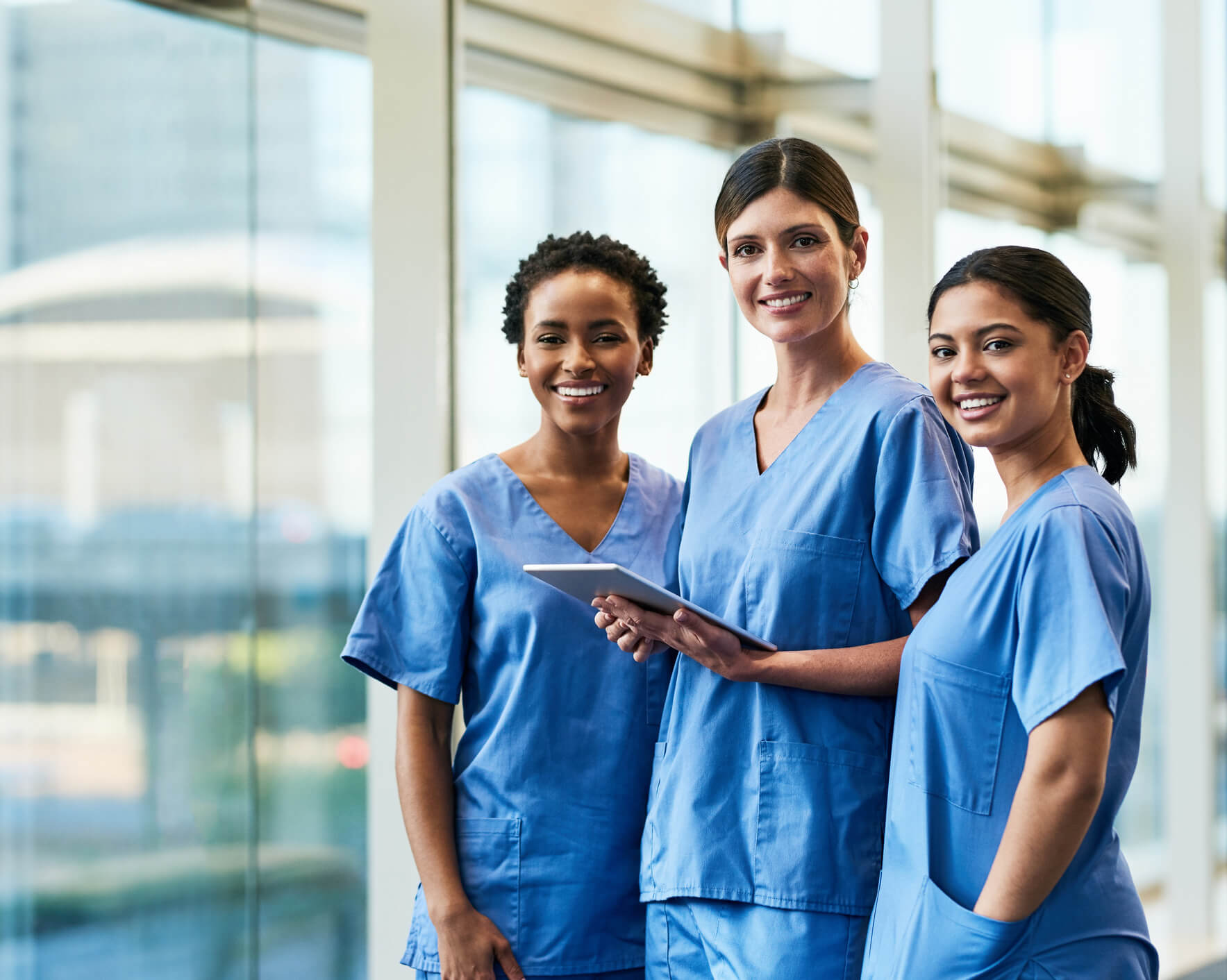 A diverse group of female nurses looking at data on a digital tablet in a hospital.