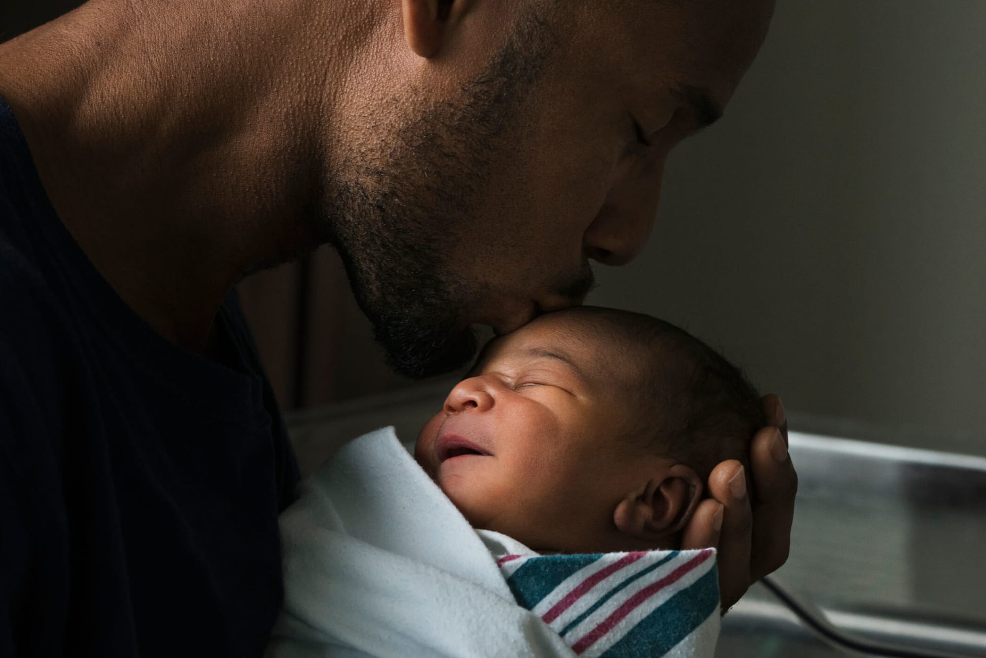 Black father kissing the forehead of his newborn son.