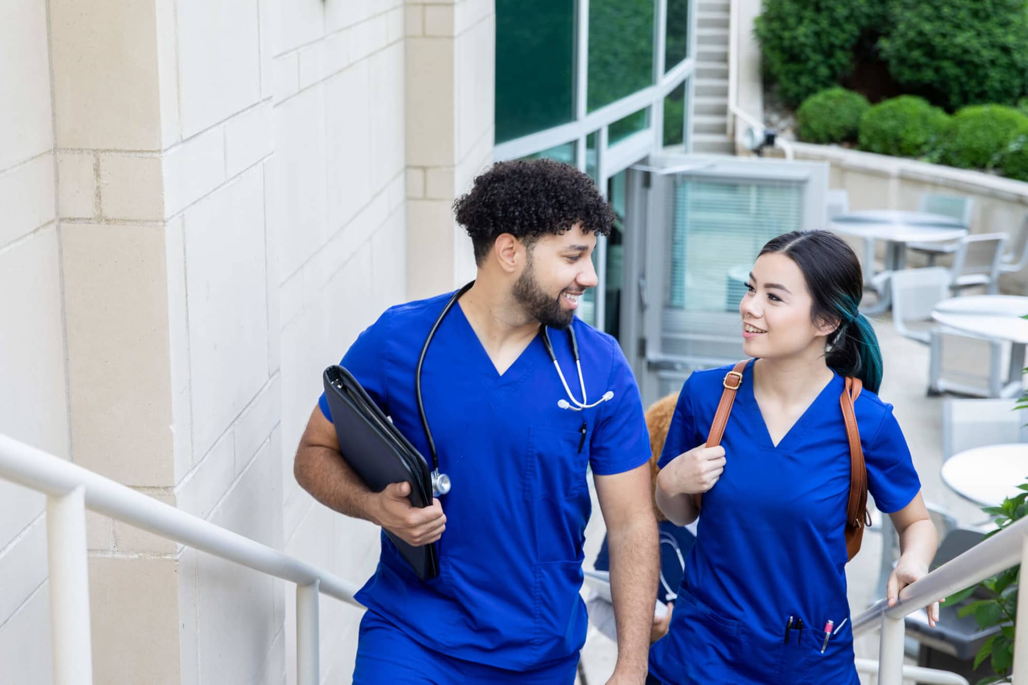 A pair of nursing students (one male and one female) are chatting while walking to class together on campus.