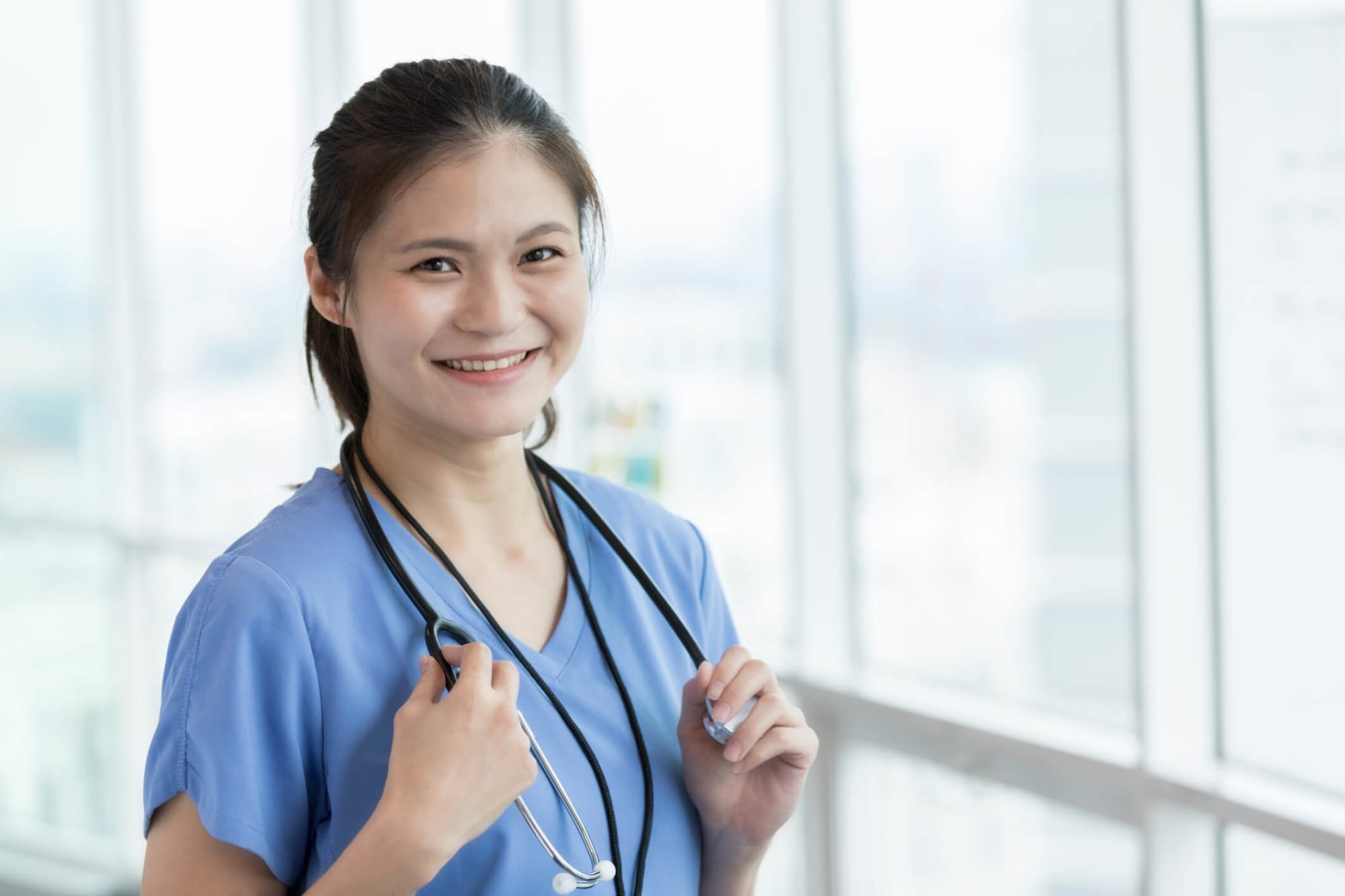 A female Asian-American nurse standing proudly and smiling for the camera in a hospital hallway.