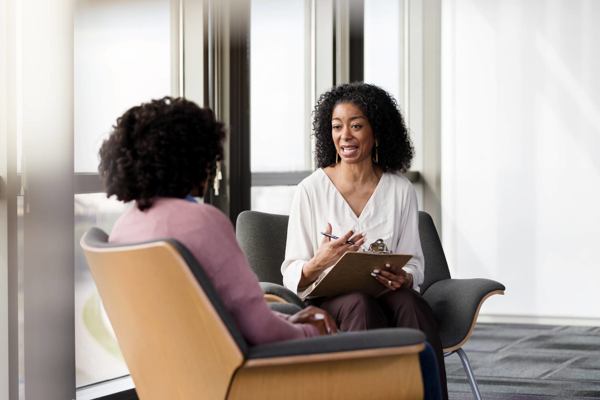 Senior Black female psychiatrist asks a female patient questions about her mental health during a therapy session.