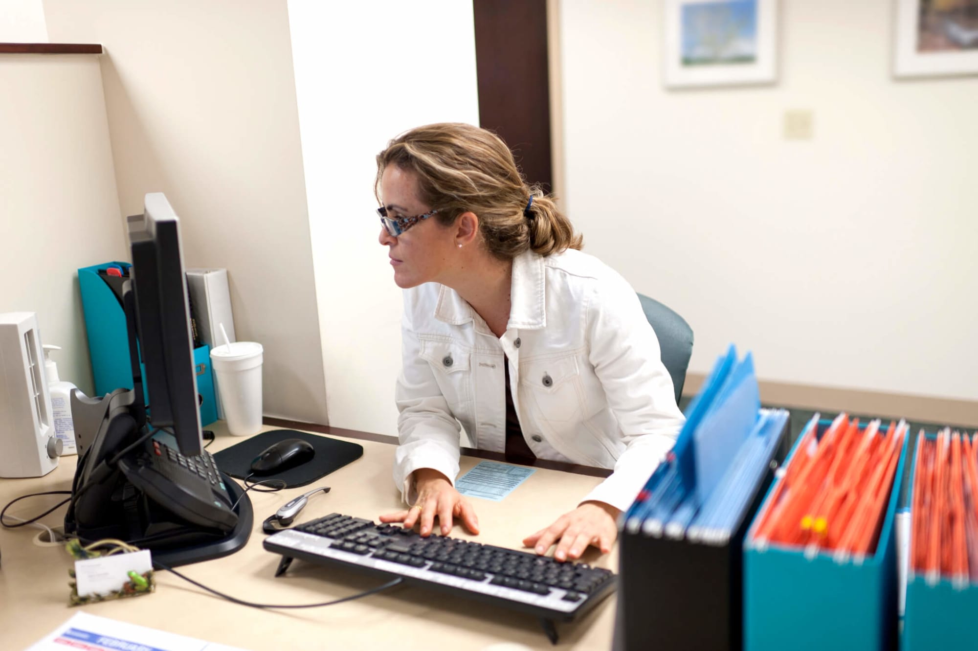 Mid-adult female administrative professional working at her desk in a nursing board office. She is looking at the computer screen while typing on the keyboard.