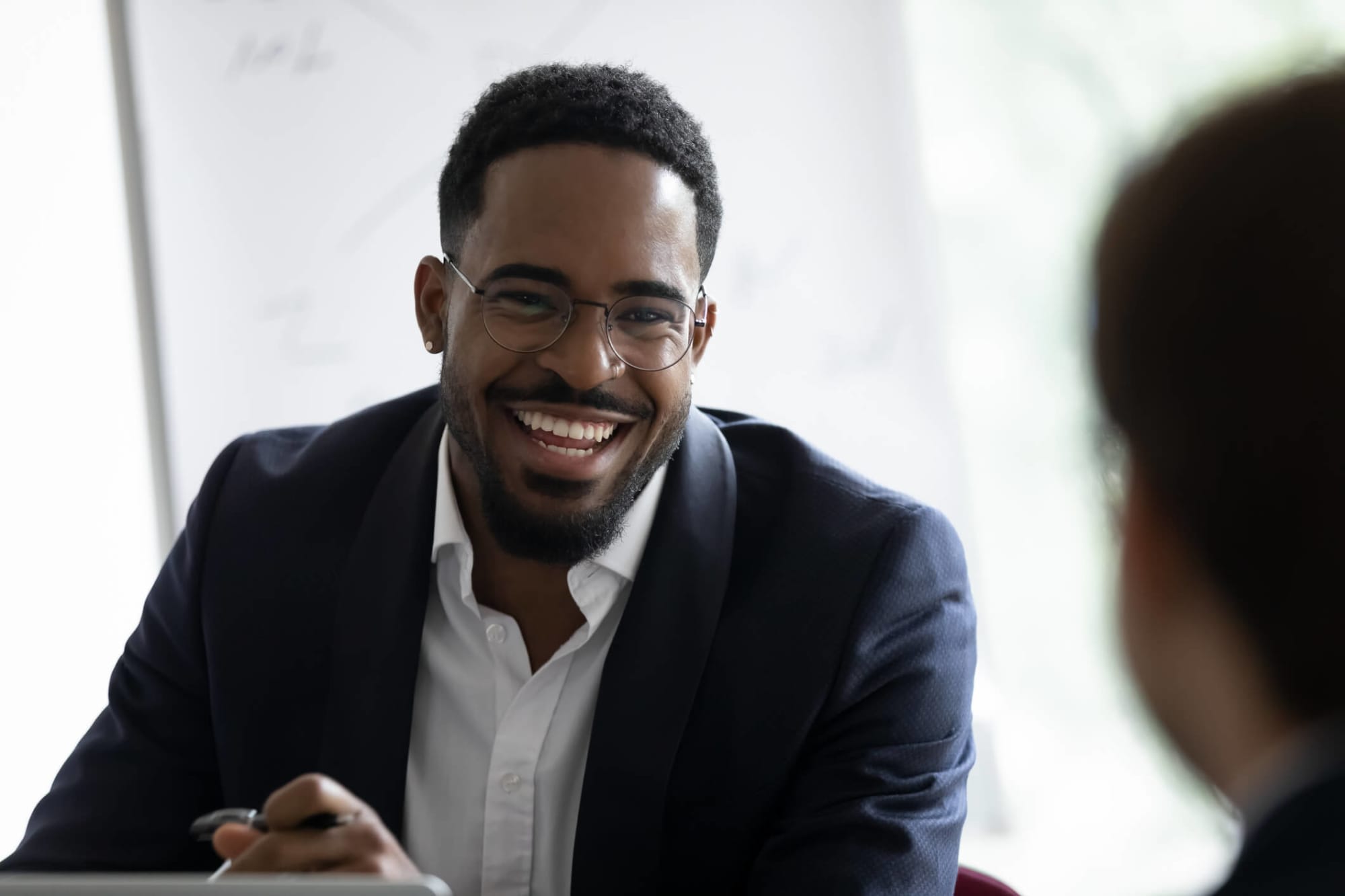 African-American male recruiter dressed in business attire. He is sitting in an office chatting with a job-seeker.