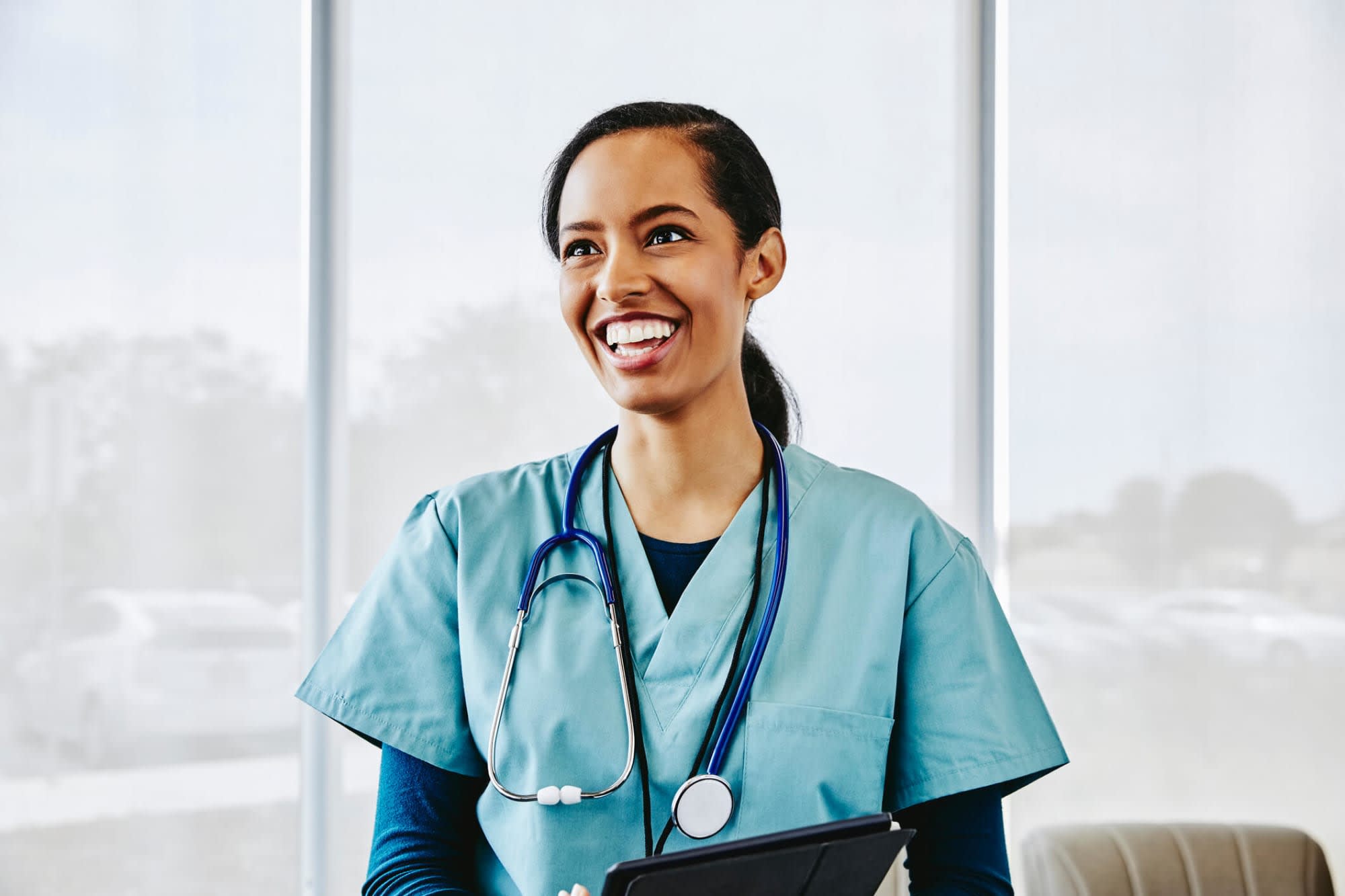 A young African-American female nurse smiling while standing in a hospital lobby.