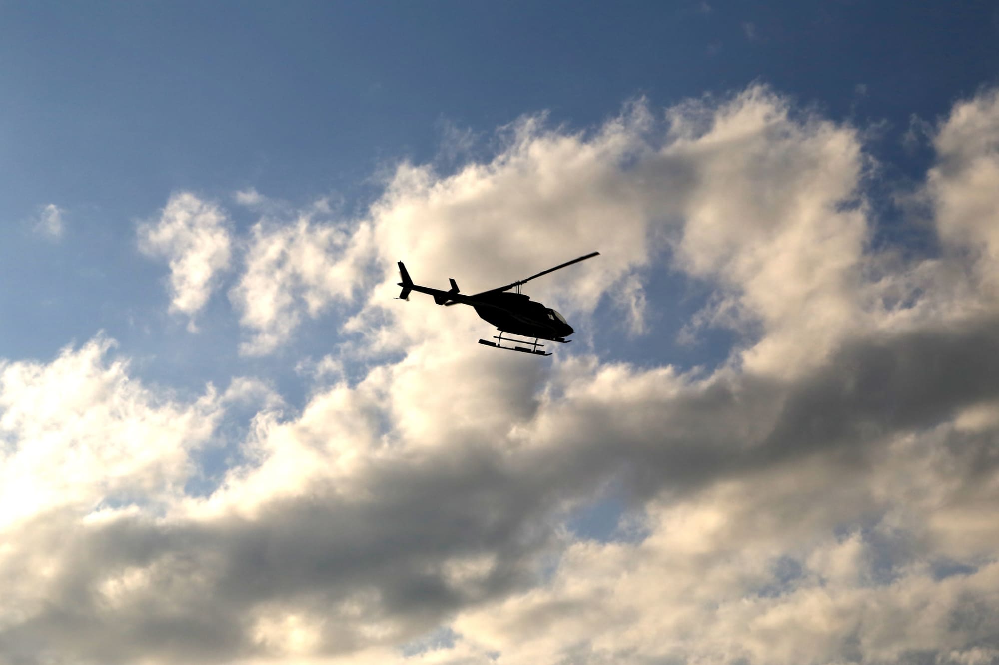 Silhouette of a medical helicopter flying in the partially cloudy sky