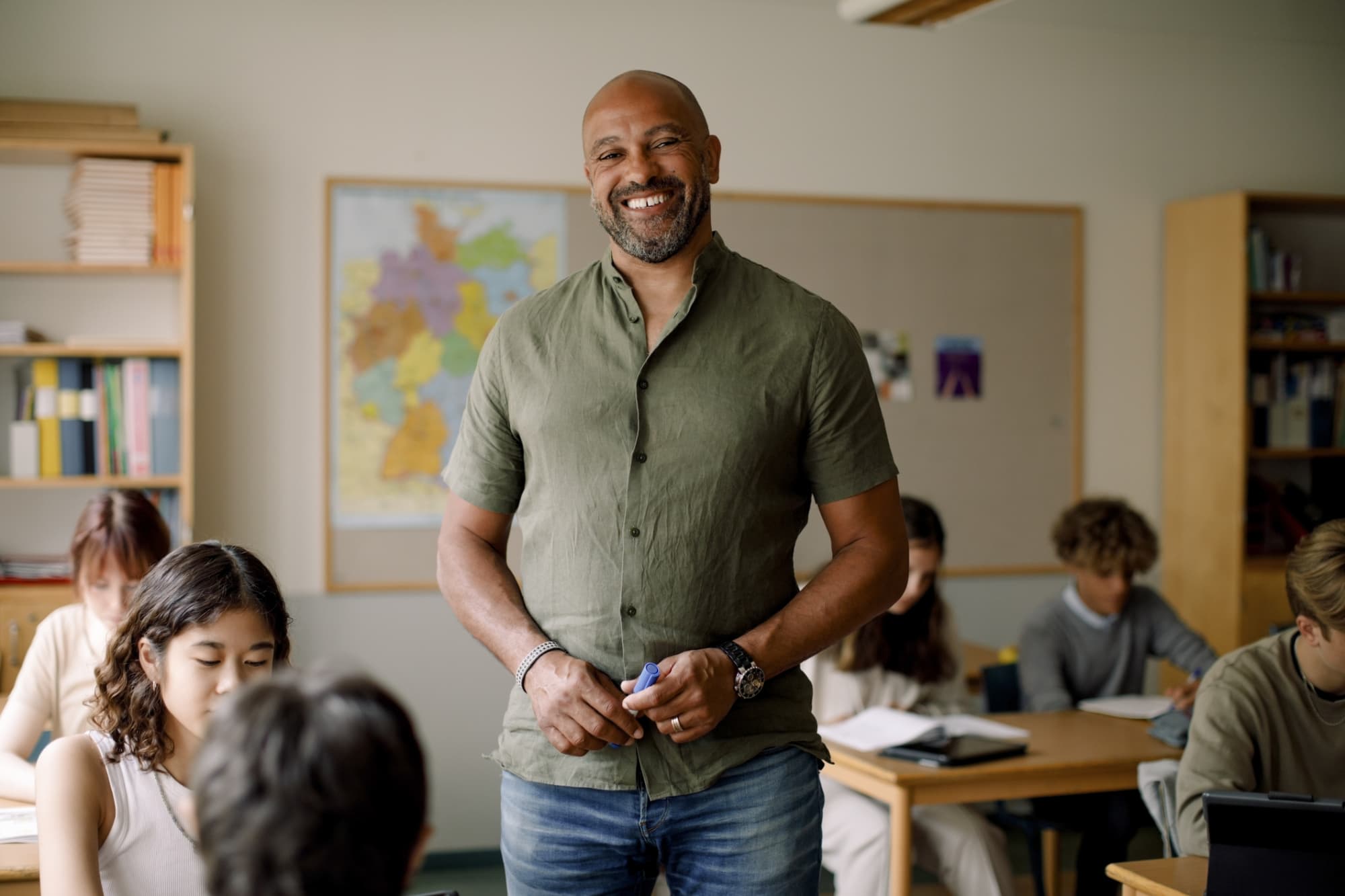 Smiling male teacher standing in classroom with students at desks