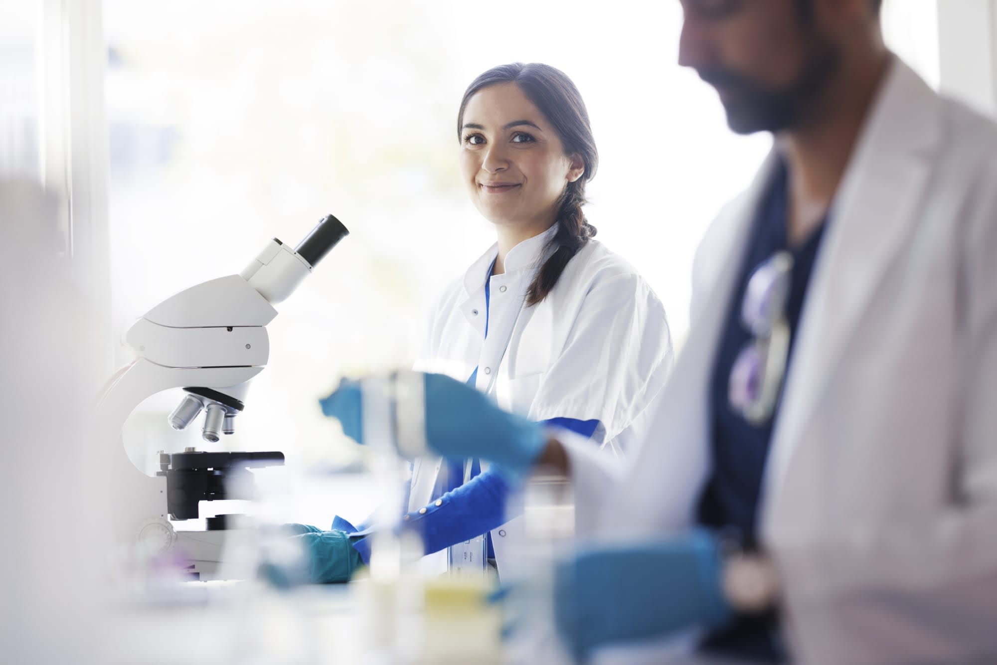 Two scientists working in a lab with a microscope wearing scrubs