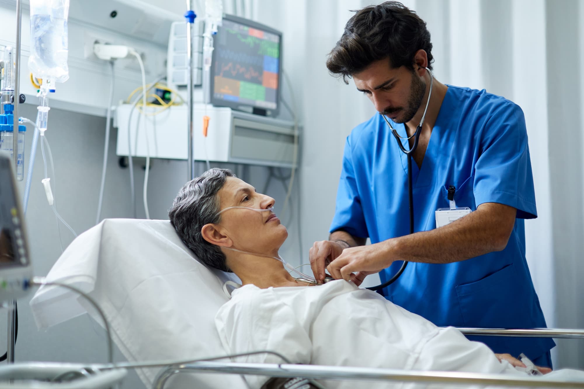 A male nurse is listening with a stethoscope the heart bit of a patient.