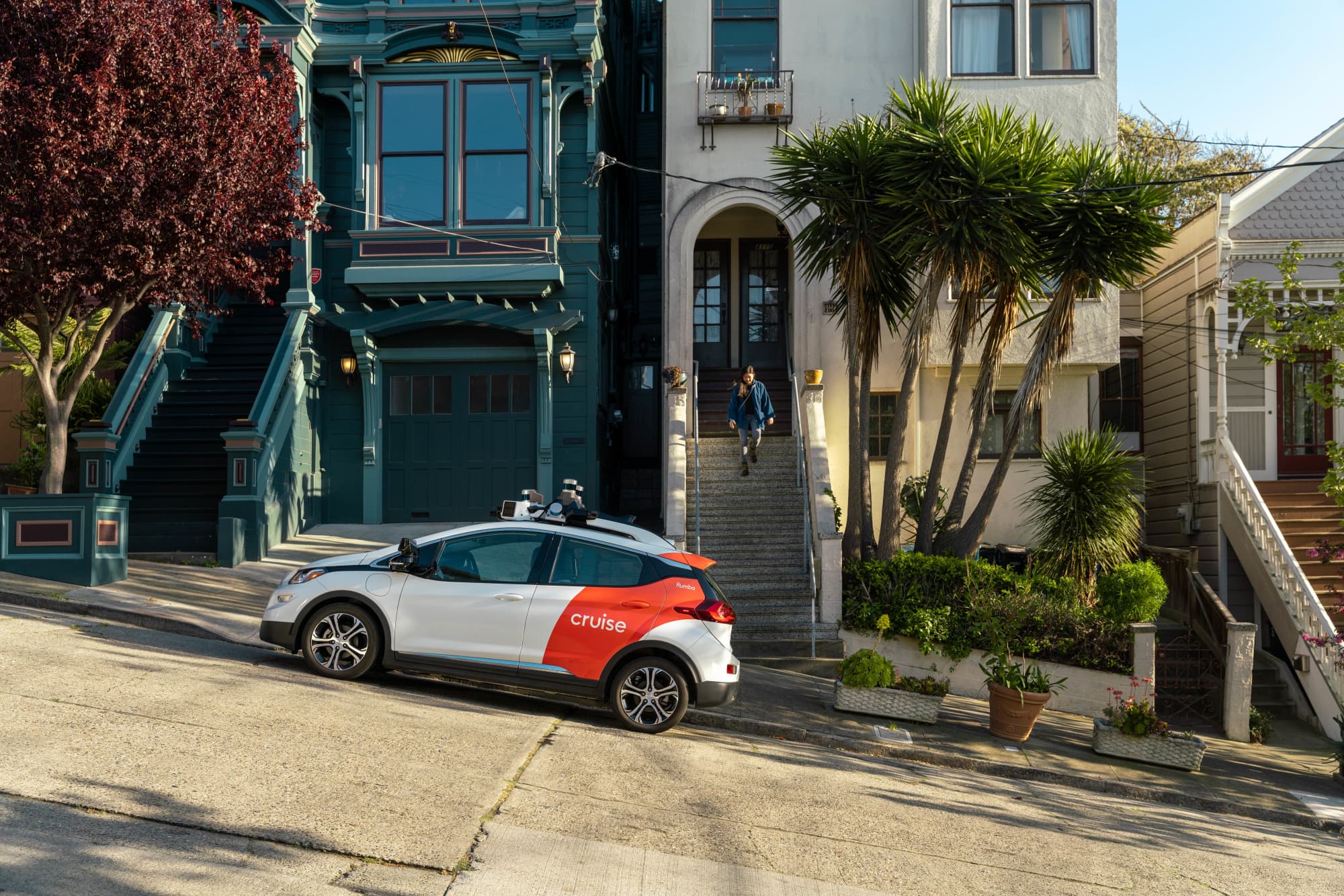 A person walking out of their house toward a Cruise car parked on the street