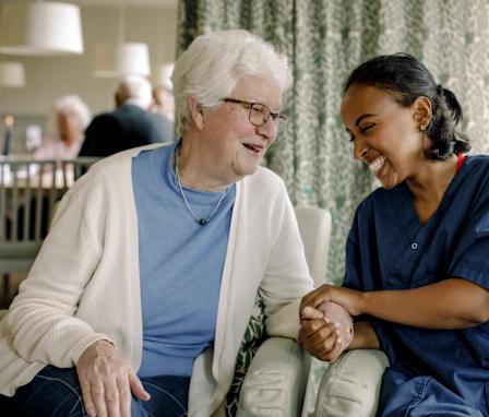 Cheerful female nurse holding hand of senior woman sitting at retirement home