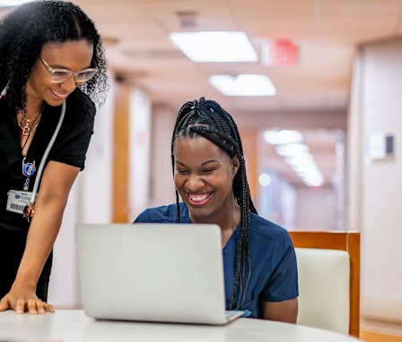 Nursing student on laptop getting help from nurse