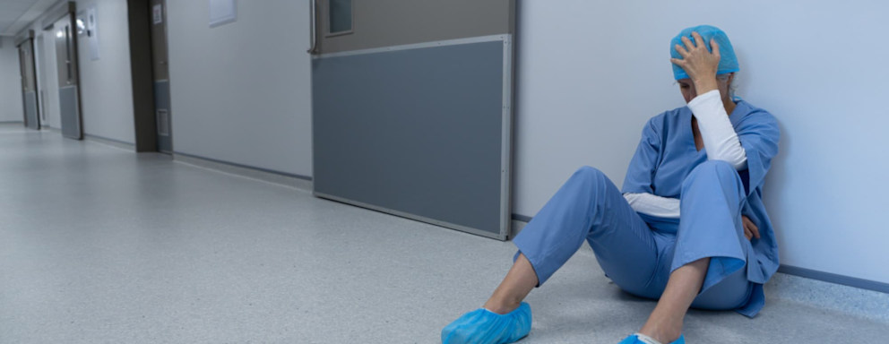 Tired nurse in scrubs sitting on hospital hallway floor