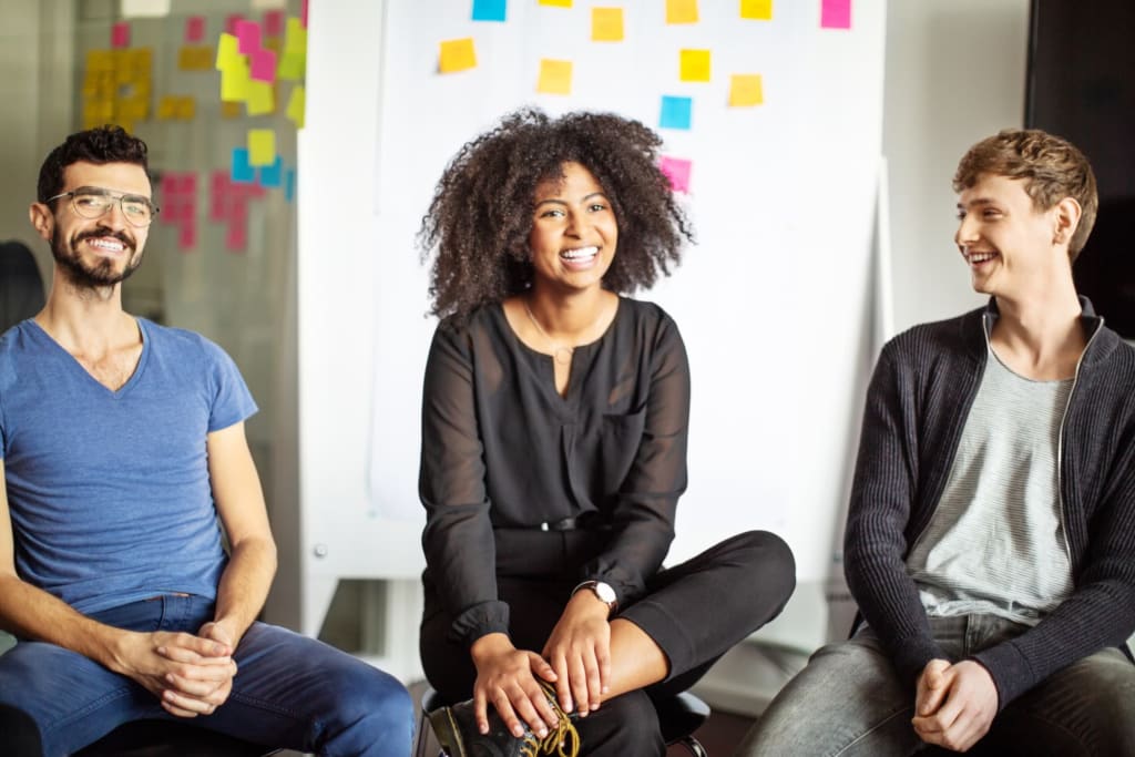Three people smiling with wall covered in sticky notes behind them