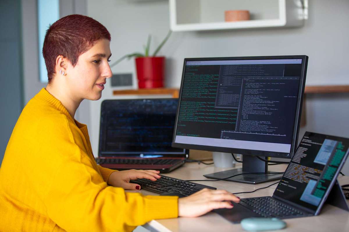 Female programmer coding on a desktop computer and laptop