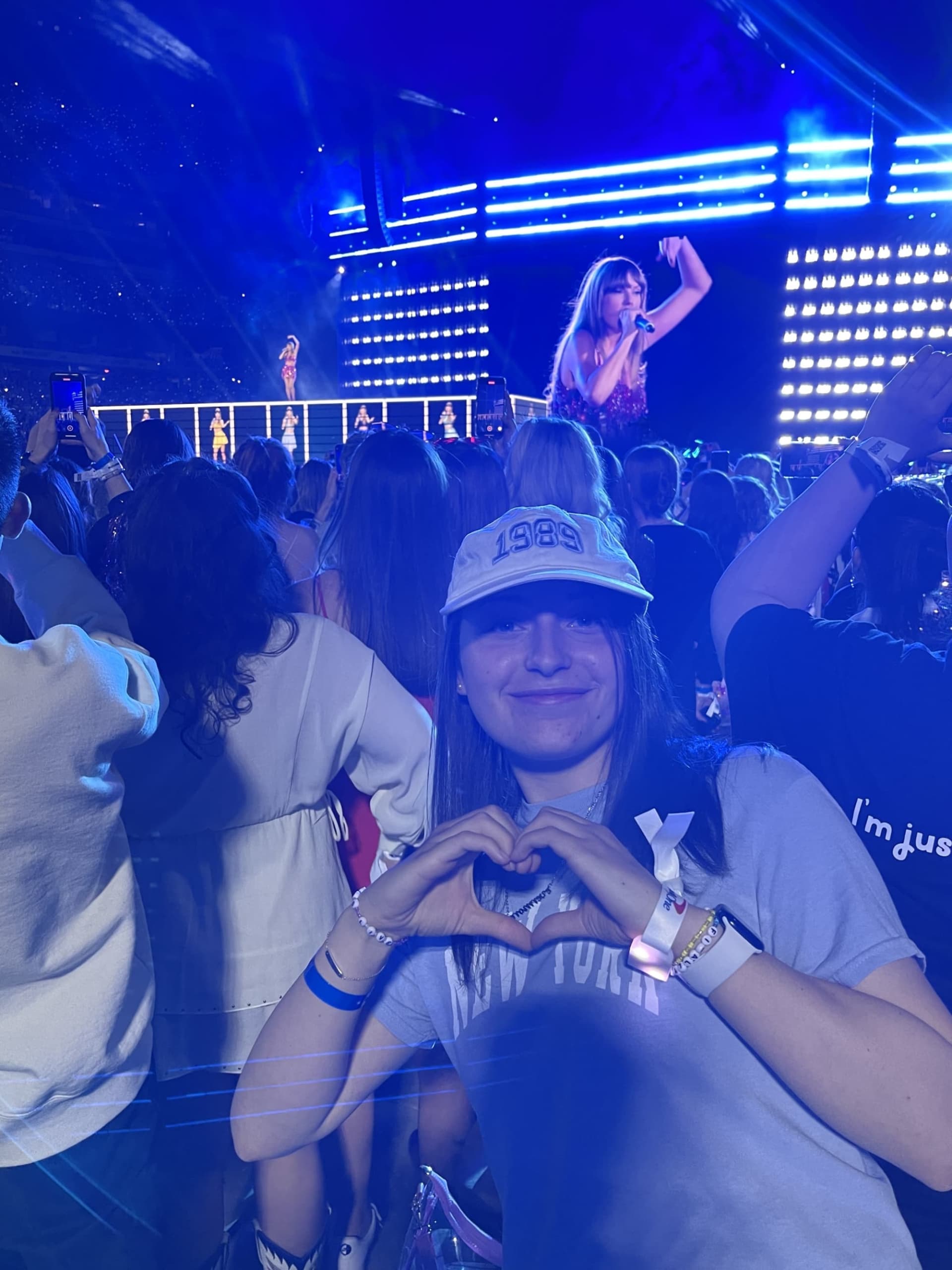 Ava Jeffs making a heart with her hands in front of Taylor Swift performing.